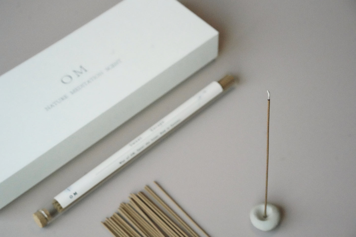 Close-up of OM incense stick tube with holder – refined floral and warm spice scent design