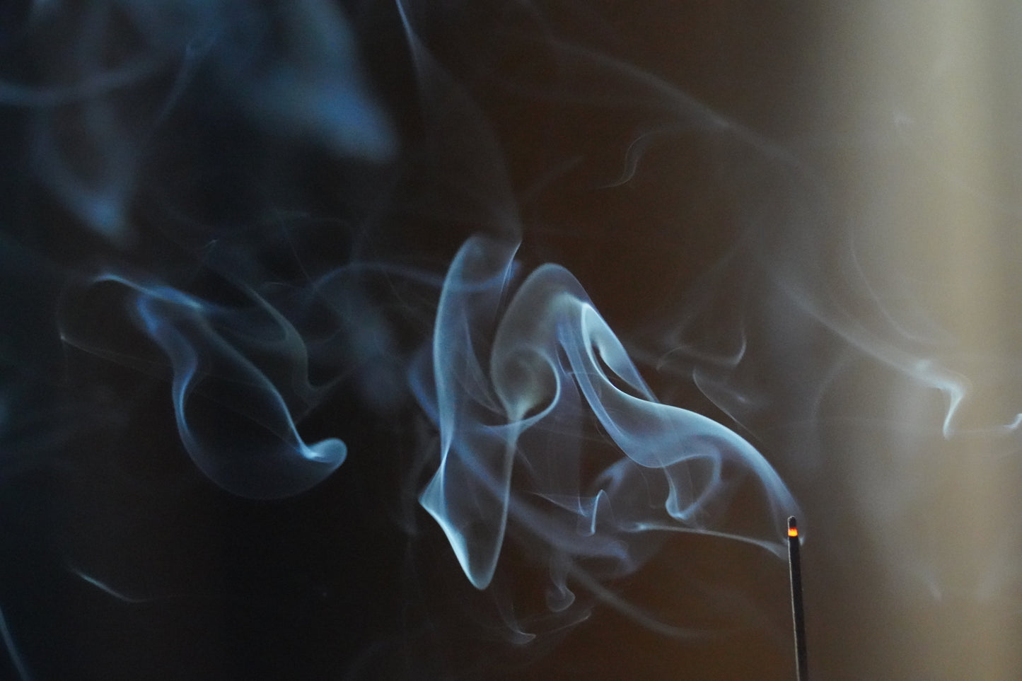 Incense smoke curling into the dark – OM ritual fragrance captured in motion