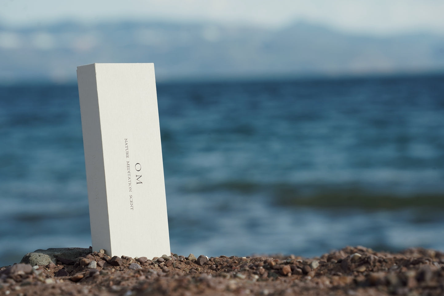 OM incense tube standing on stone with ocean in background – Floating Sea scent inspired by sacred sea breeze