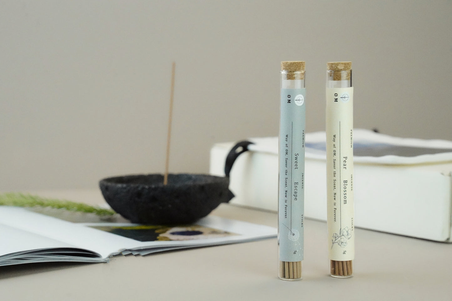 Natural incense burning on black volcanic holder with pear blossom and sweet escape sticks, minimalist scene with plant background