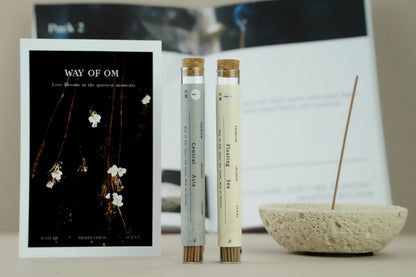 Burning incense on cream white holder with OM ritual card and gift box – warm ambient setting