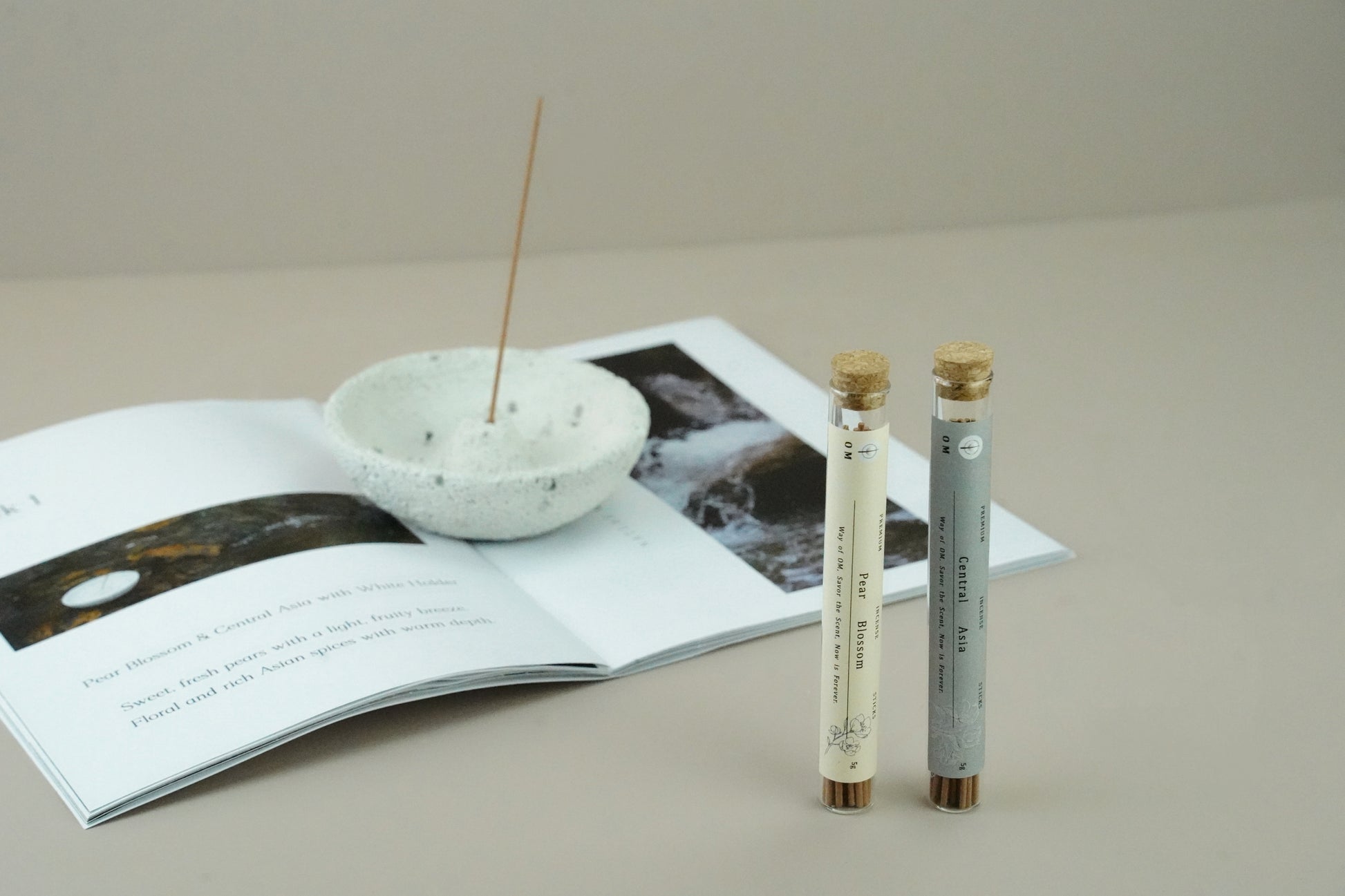White volcanic incense holder with burning sticks on white table – OM ritual fragrance set with Pear Blossom and Central Asia